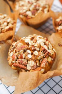 Close-up of a bakery-style pumpkin maple pecan muffin topped with oat-pecan streusel in a parchment liner