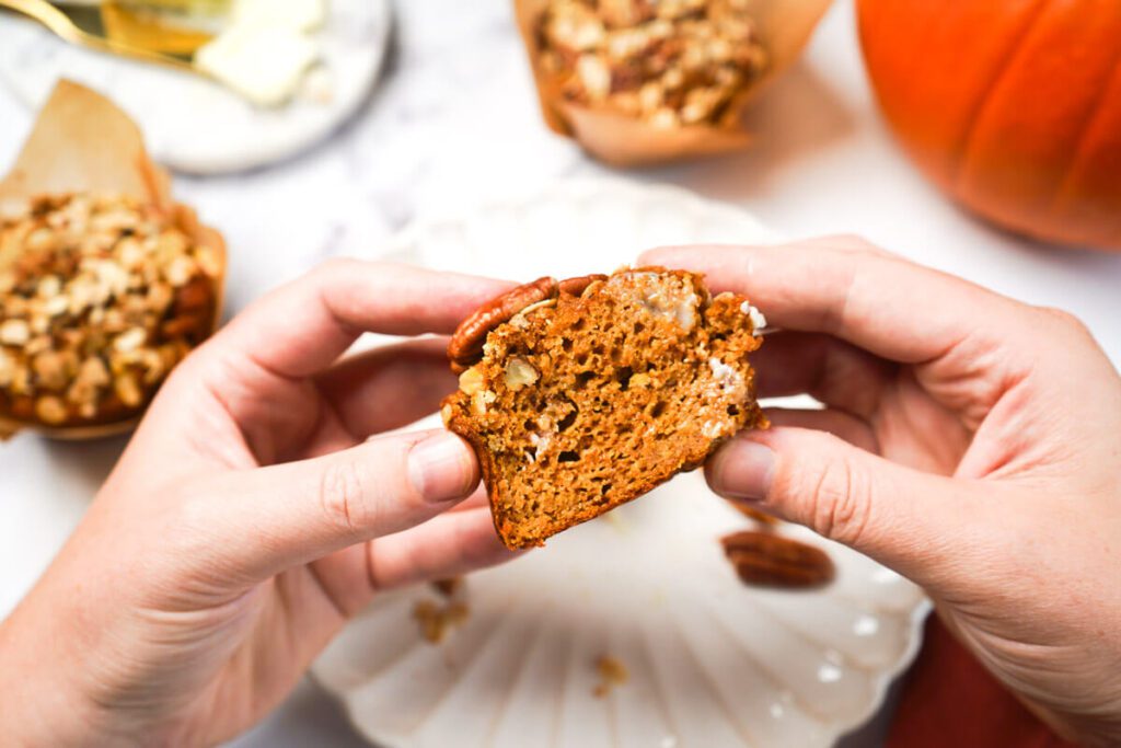 Hands pulling apart a pumpkin maple pecan muffin to show the soft, moist crumb