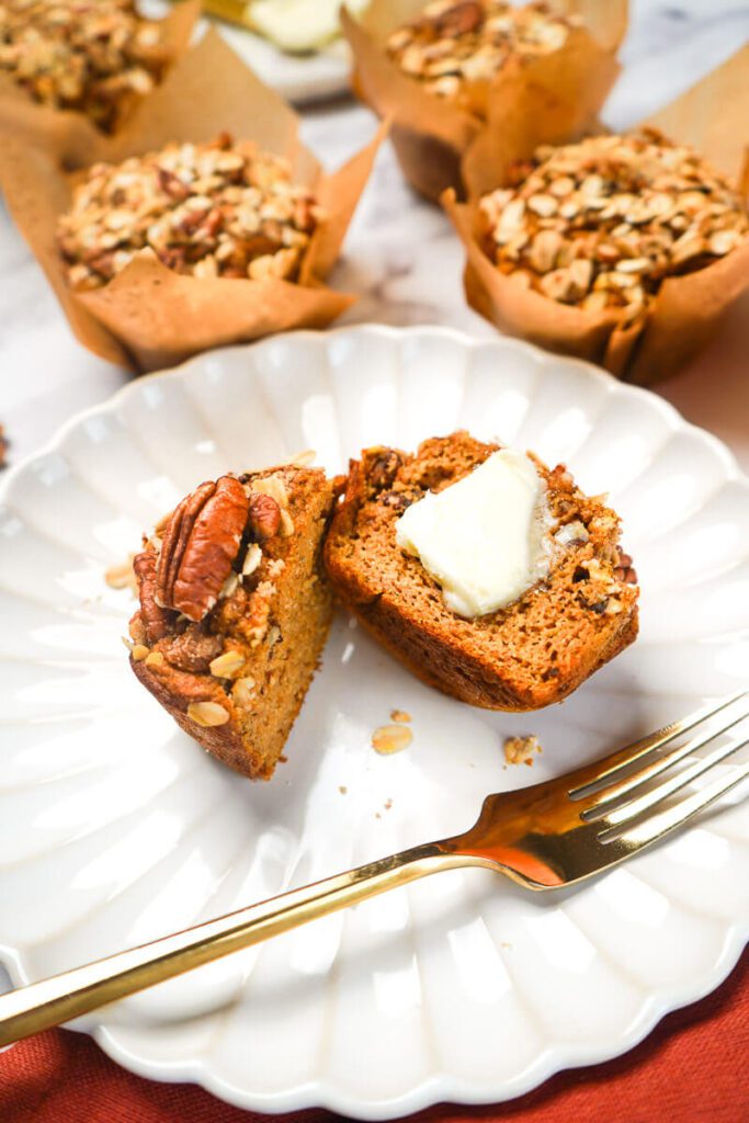 Pumpkin maple pecan muffin cut in half on a white plate with a pat of butter and a gold fork