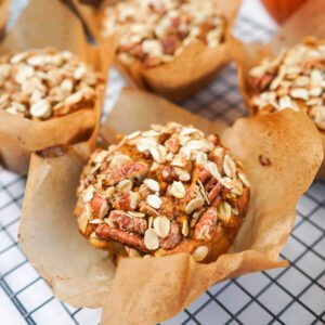 Close-up of a bakery-style pumpkin maple pecan muffin topped with oat-pecan streusel in a parchment liner