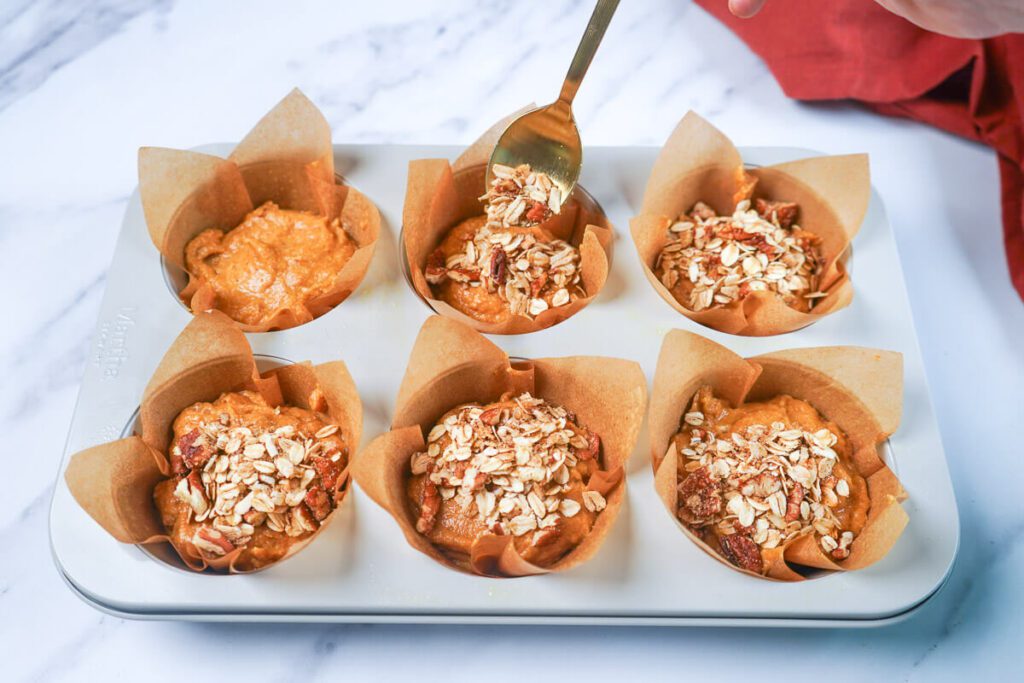 Topping jumbo muffins in parchment liners with oat-pecan streusel, ready to bake