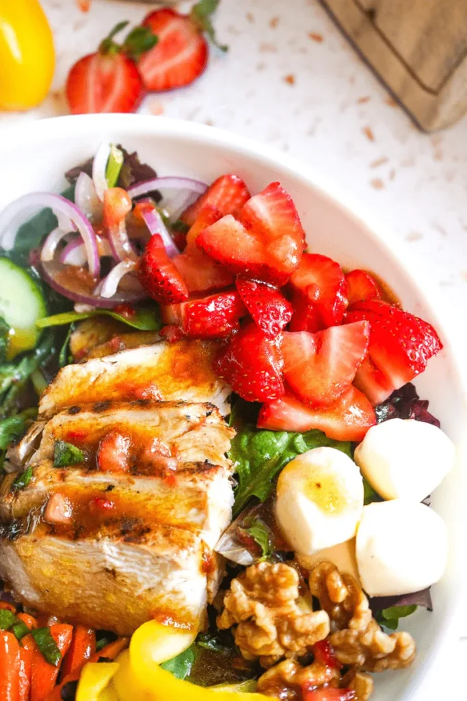 Close up shot of sliced grilled chicken, fresh strawberries, and mozzarella pearls drizzled with house balsamic.