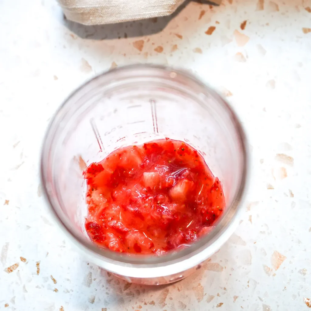 Fresh strawberries mashed in a glass jar to make homemade strawberry balsamic dressing.