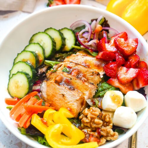 Finished strawberry balsamic grilled chicken salad plated in a white bowl with a fork.