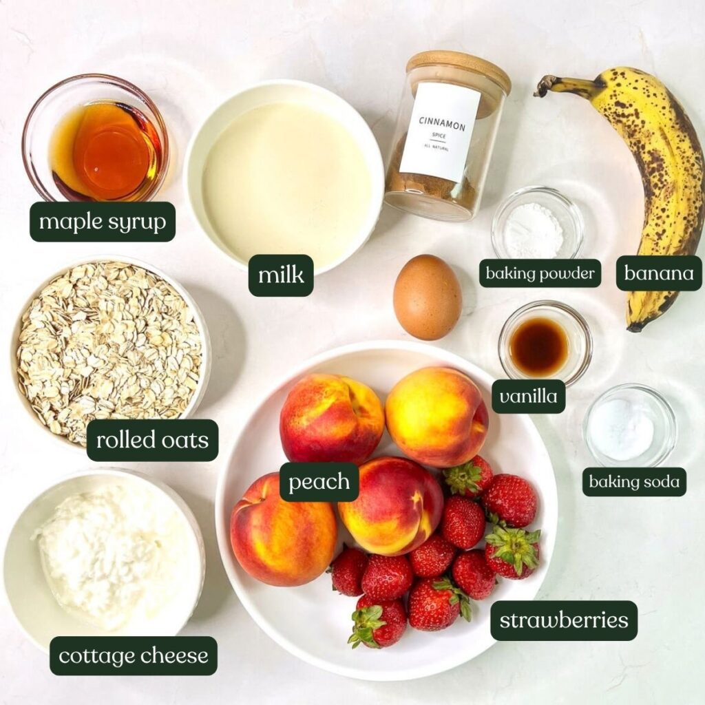 Overhead flat lay of ingredients for blended baked oatmeal including rolled oats, peaches, strawberries, cottage cheese, soy milk, maple syrup, and an egg.